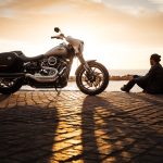 Sécuriser son garage pour mieux protéger sa moto homme-assis-sur-le-sol-a-cote-de-la-moto-de-voiture-de-croisiere-argentee-garee-1HZcJjdtc9g